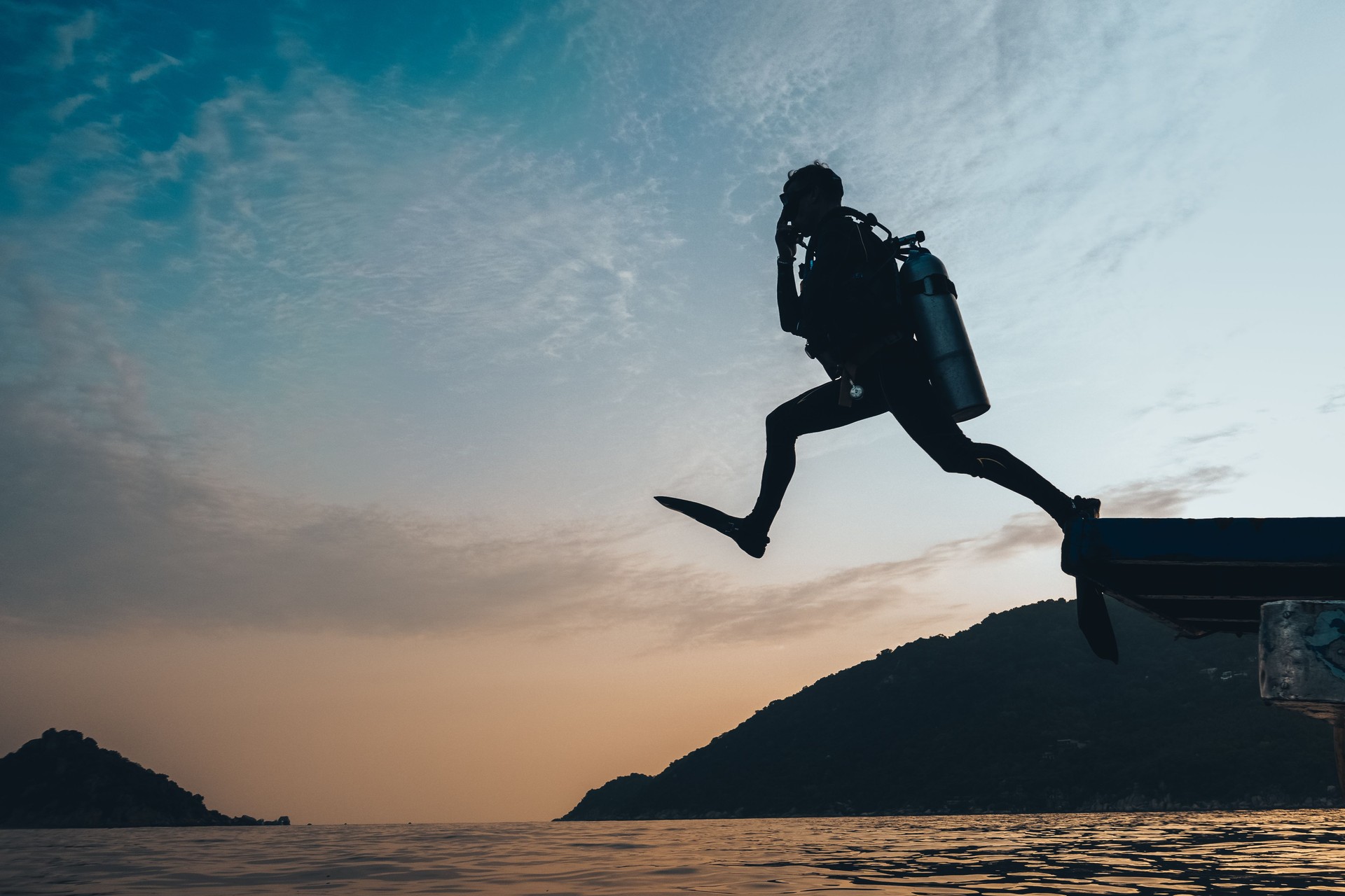 a Silhouette of Scuba Diver Jumping to the open ocean on a sunrise